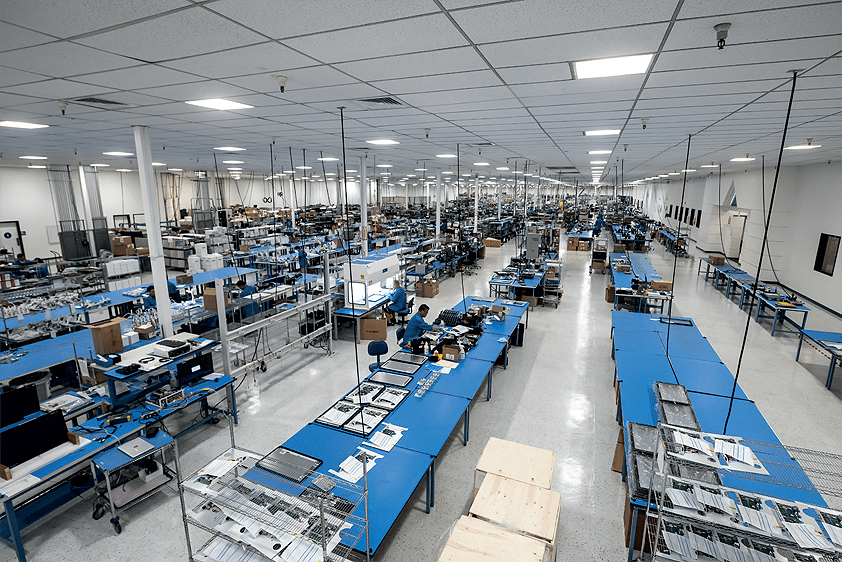 A large electronics manufacturing facility with workers assembling circuit boards, facing uncertainty due to pending tariffs.